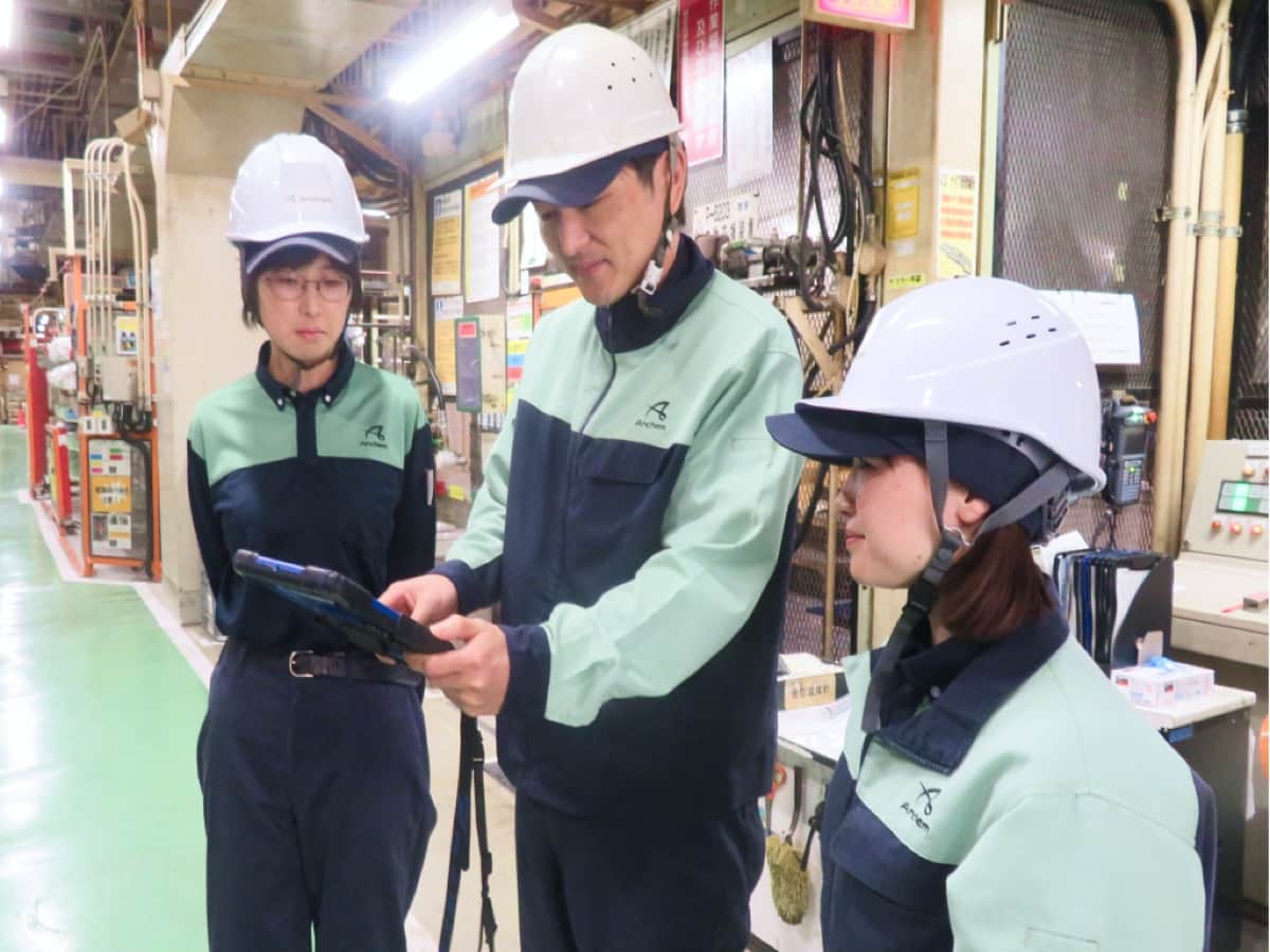 工場内でタブレットを見ながら作業する社員たち