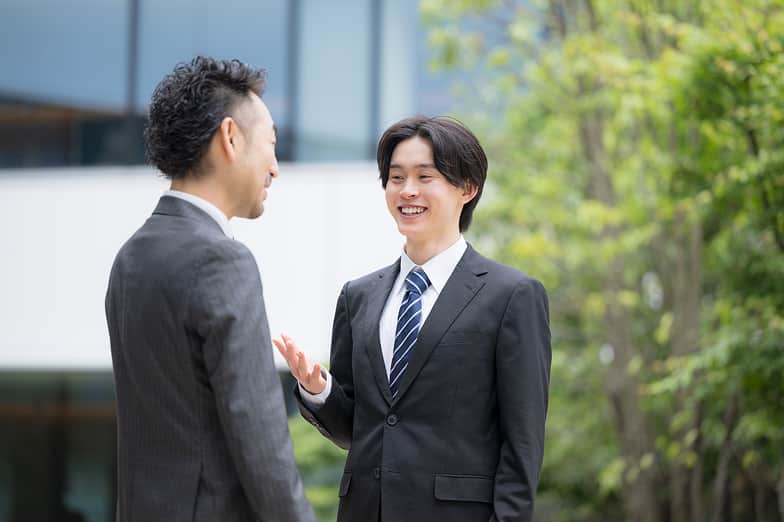 スーツ姿の社員同士が屋外で会話する様子
